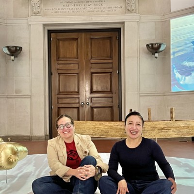 Two people sit smiling inside a gallery space