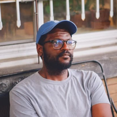 Man wearing glasses and a blue cap sitting on a bench by a window.