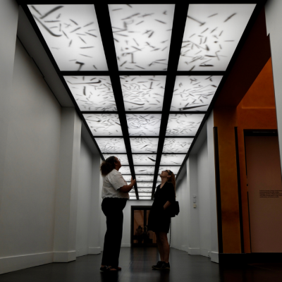 Two people stand under a patterned, backlit ceiling in a modern hallway.