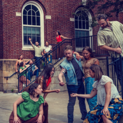 A group of people interact on a sidewalk and stairs outside a red brick building