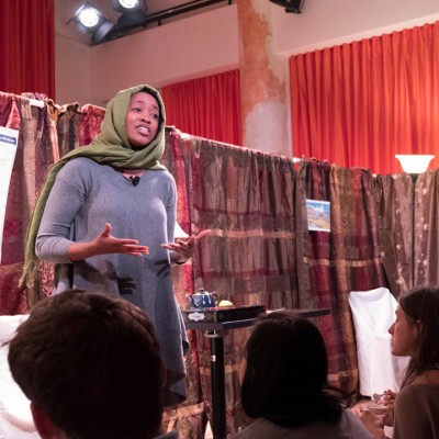 A woman with her head covered in a green scarf speaks before a crowd in a bookstore