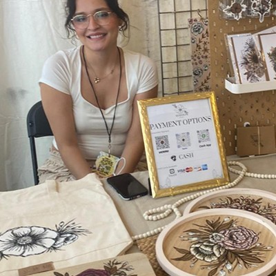 Smiling brunette woman sitting at a booth surrounded by artwork