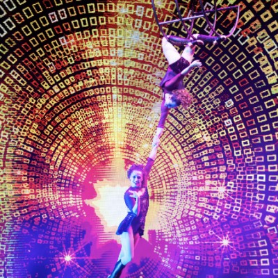 Acrobatic performers pose for a photo on stage, while surrounded by intense theatrical lights