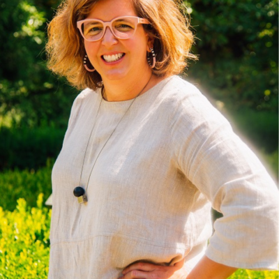 Woman with short hair and glasses smiling outdoors in sunlight