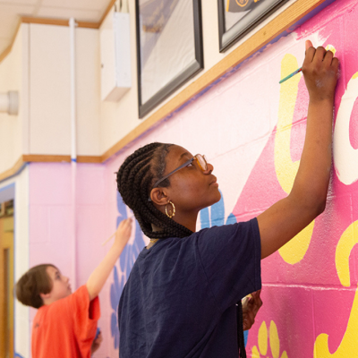Two people painting large, colorful letters on a wall mural