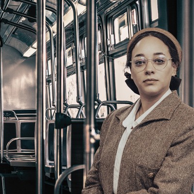 A sepia-toned photograph of a woman dressed in old fashioned clothing sitting inside a bus