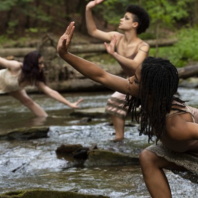 Three dancers stretch their arms and legs, dramatically posing in a river scene