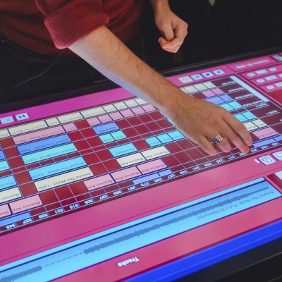 A white hand adjusts a setting on a colorful, lit-up DJ soundboard