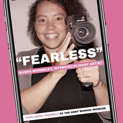 A phone screen showing a smiling Black woman holding up a camera. The word "fearless" is typed on top of the image