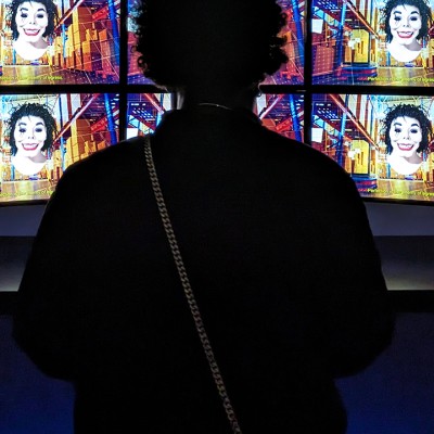 A silhouette of a woman looking at a row of brightly colored tv screens depicting a distorted Michael Jackson-esque figure