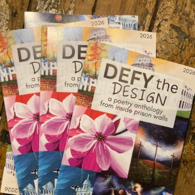 Three copies of a 2026 poetry anthology titled Defy the Design featuring floral cover art