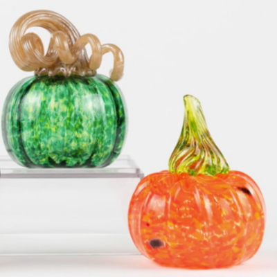 A green glass pumpkin with a curly stem next to a smaller orange glass pumpkin.