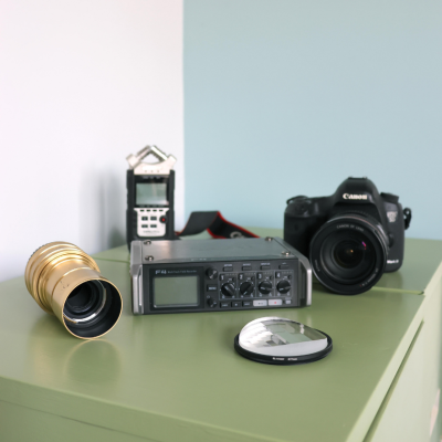 A camera, lens, audio recorder, audio mixer, and filter on a green surface.