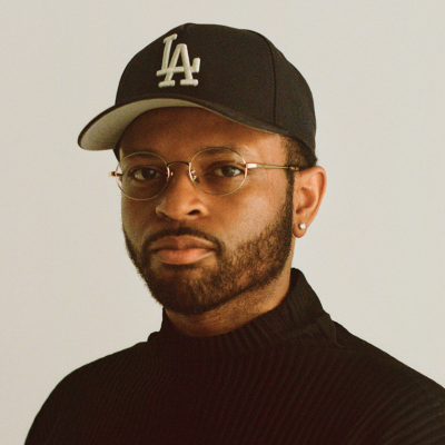 Man in glasses and a black LA cap wearing a black turtleneck, facing forward.