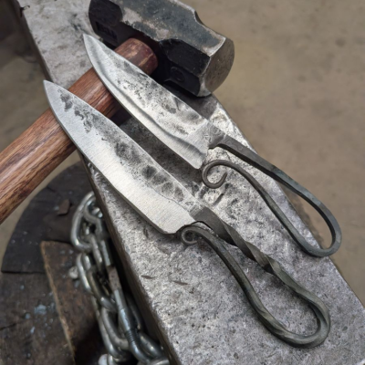 Two hand forged knives sitting on a metal surface.