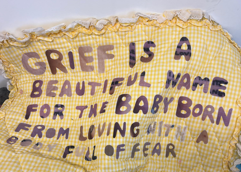 Yellow quilt with hand-sewn text about grief being a beautiful name for a baby born of fear