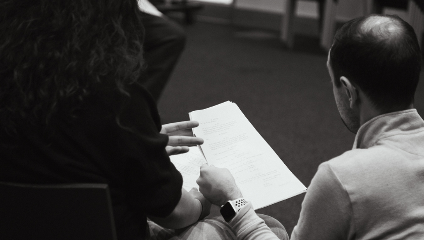Two people sit and look at a script or document together.