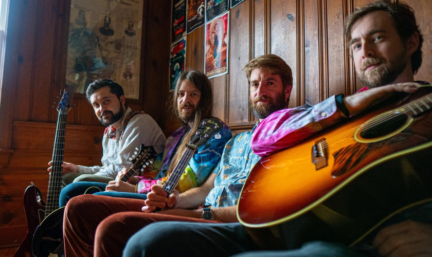 Four men sitting with string instruments in a wood-paneled room.