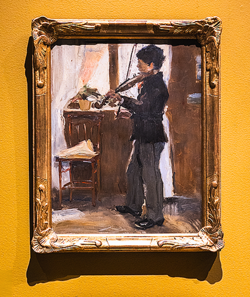 Framed painting of a person playing violin next to a chair on a yellow wall.