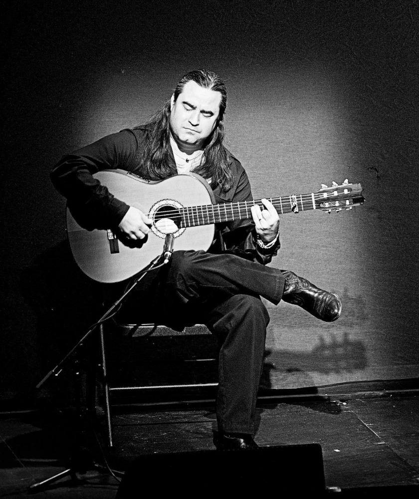 A man plays acoustic guitar on stage, lit by a spotlight.