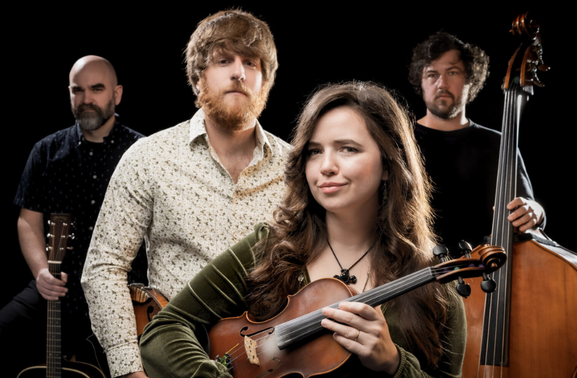 Four musicians pose against a black background. The woman in front holds a violin, while the three men behind her hold a guitar, double bass, and have a relaxed yet focused demeanor.