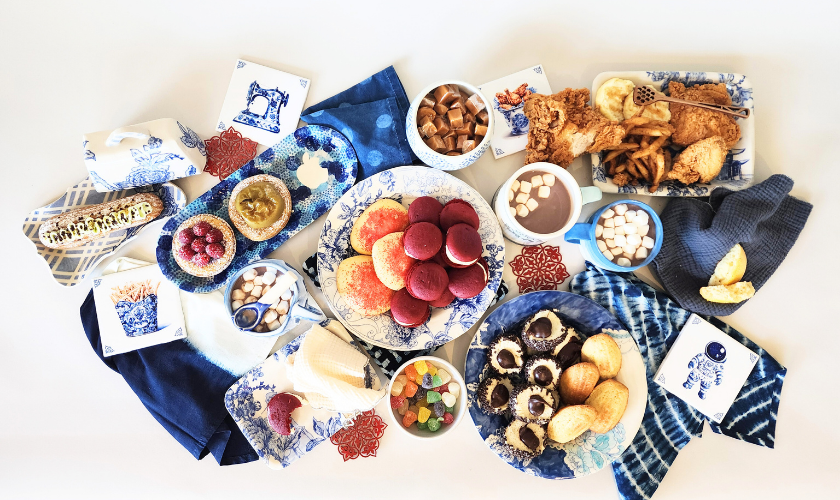 A festive spread on a tabletop with that holds beautiful dinnerware, pastries, fruit and hot chocolate.