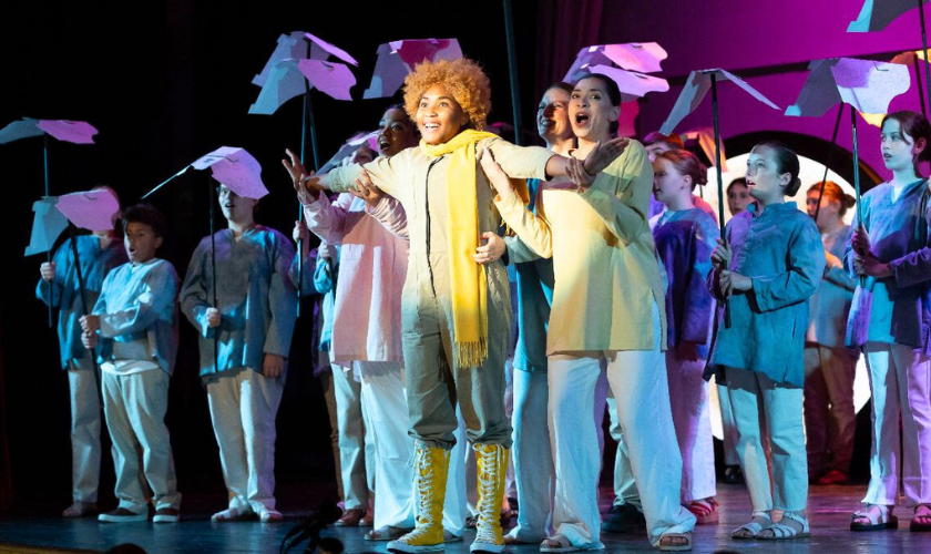A group of performers sings on stage holding props shaped like birds.