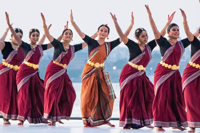 Women perform a traditional Indian dance in colorful sarees and gold jewelry.