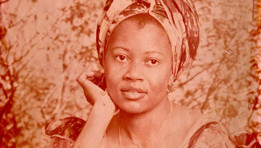 Woman in traditional headwrap and dress posing for a portrait in sepia tone.