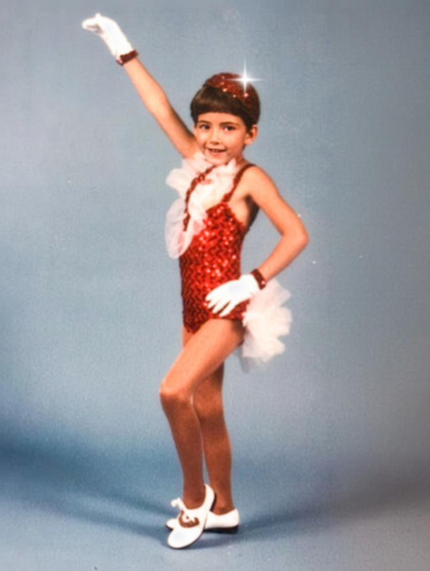 Young child in a red sequin dance costume posing with one arm raised.