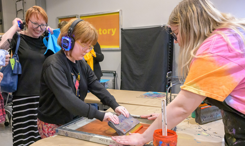 Three people work together on a screen printing project in a classroom setting.