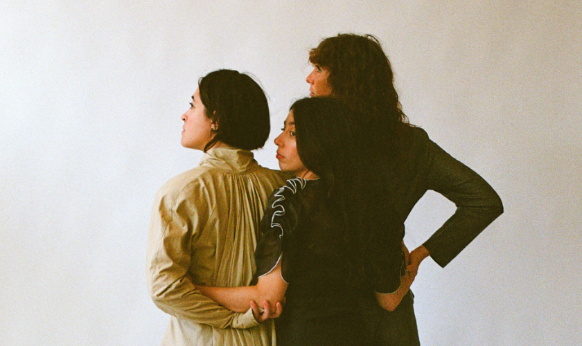 Three people in different outfits stand close together, facing away from the camera.