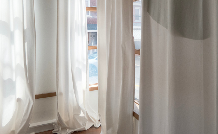 White curtains hanging by a window with soft daylight shining through.