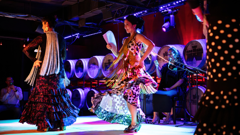 Flamenco dancers in colorful dresses performing on a stage with dramatic lighting.