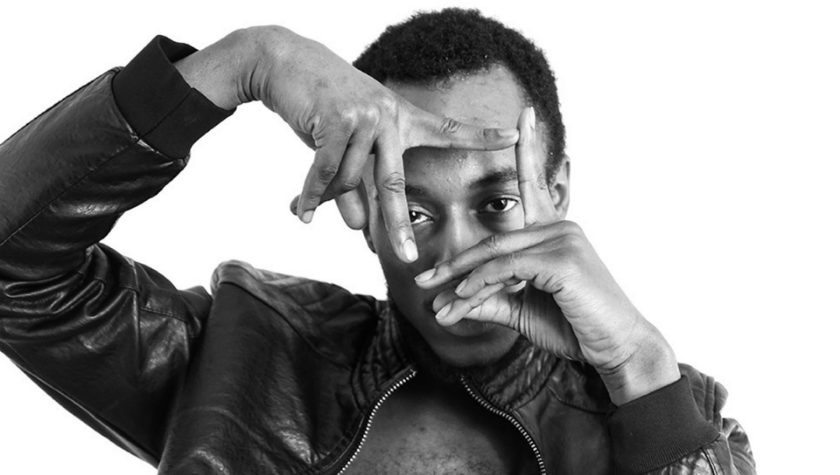 Man in a leather jacket framing his face with his hands against a white background.