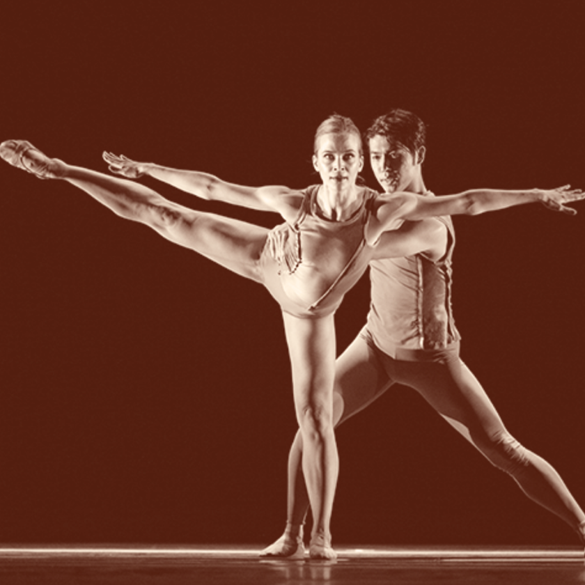 Two ballet dancers pose gracefully on stage, one with a leg extended high to the side.