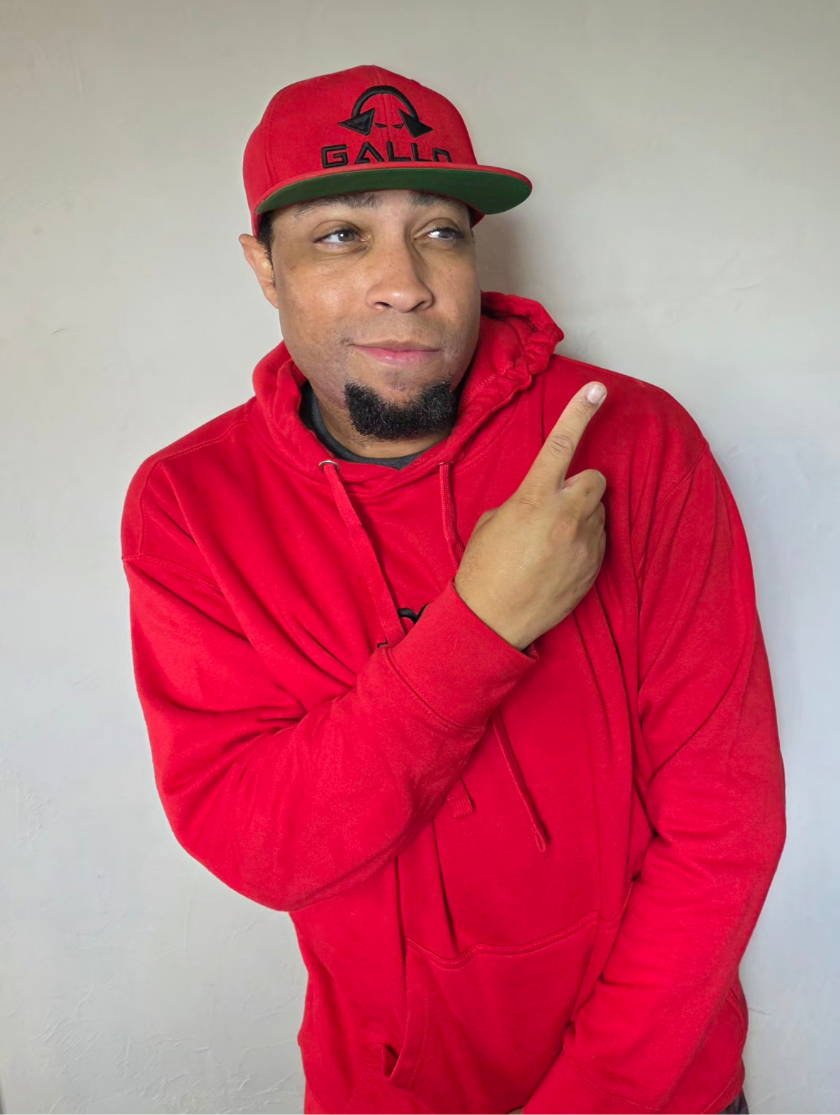 Man in a red hoodie and cap pointing to his right with a playful expression.