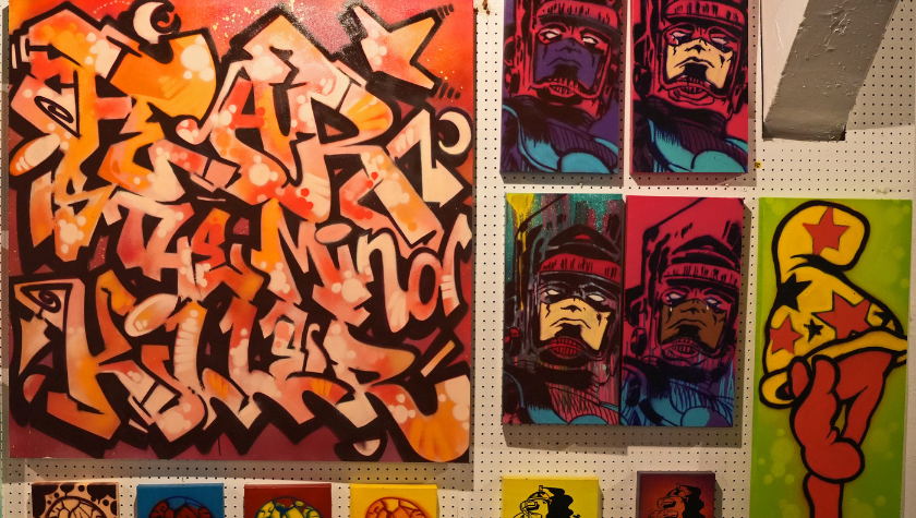 Colorful graffiti and comic-style art pieces displayed on a wall with a pegboard background.