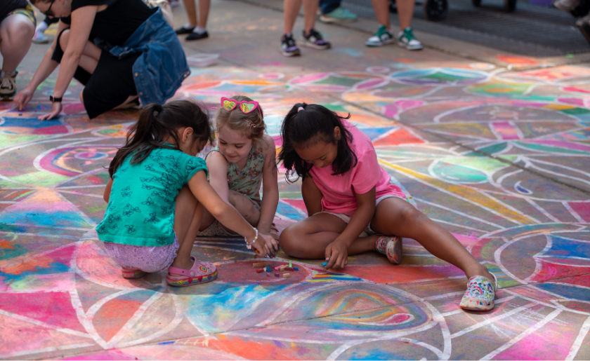 Three kids draw with chalk on a colorful sidewalk during an outdoor art activity.