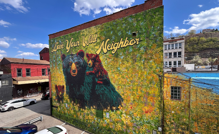 Mural of two bears in a field with the text “Love Your Wild Neighbor” on a building wall.