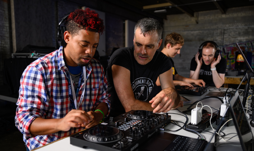 	 Two people using DJ equipment, while two others work at laptops in the background.