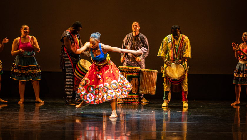 A group performs a vibrant African dance on stage with colorful costumes and drums.
