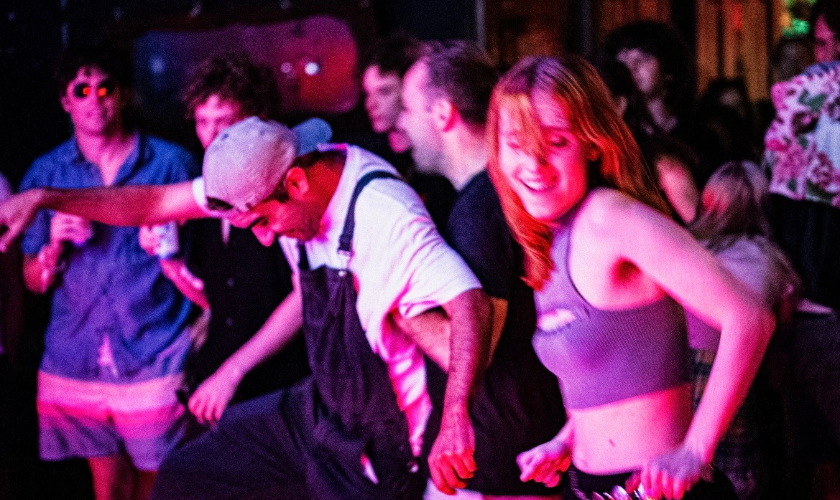 People dancing energetically in a vibrant, dimly lit venue with colorful lights all around.
