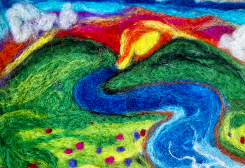 Colorful felt art of a river winding between green hills, with a sunset and clouds above.