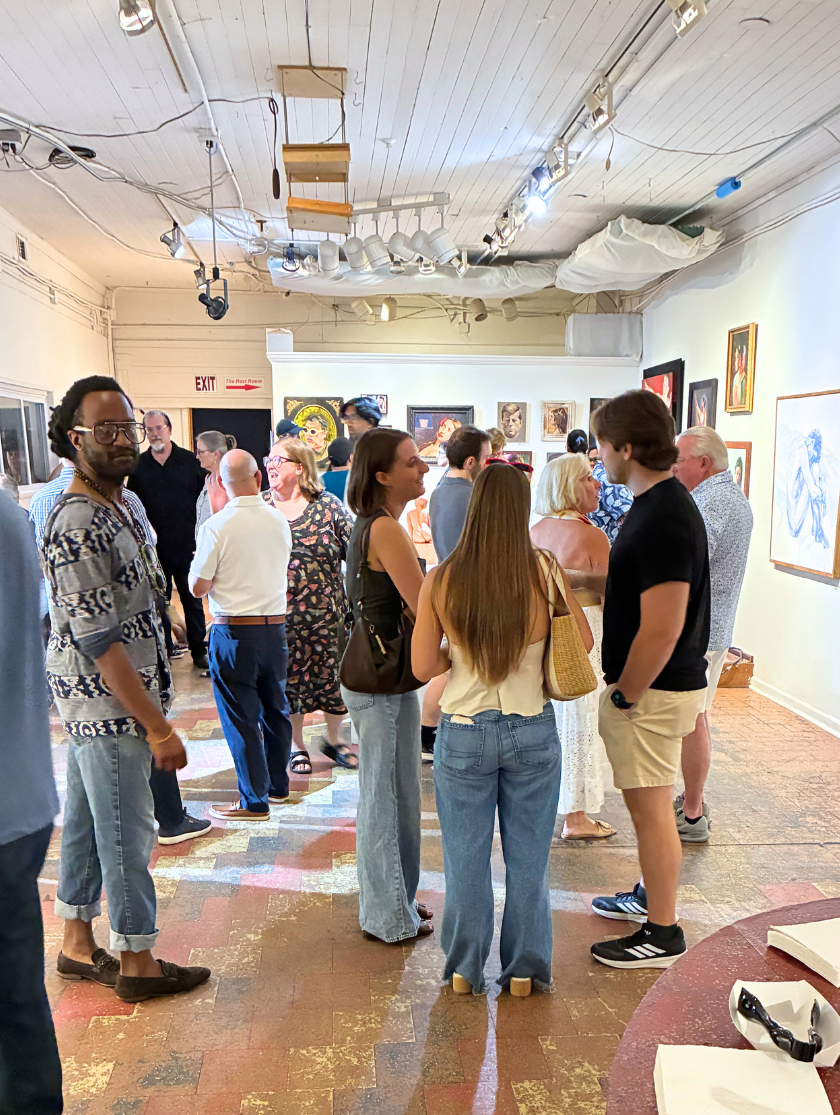 People gather in an art gallery, viewing and discussing displayed paintings on the walls.