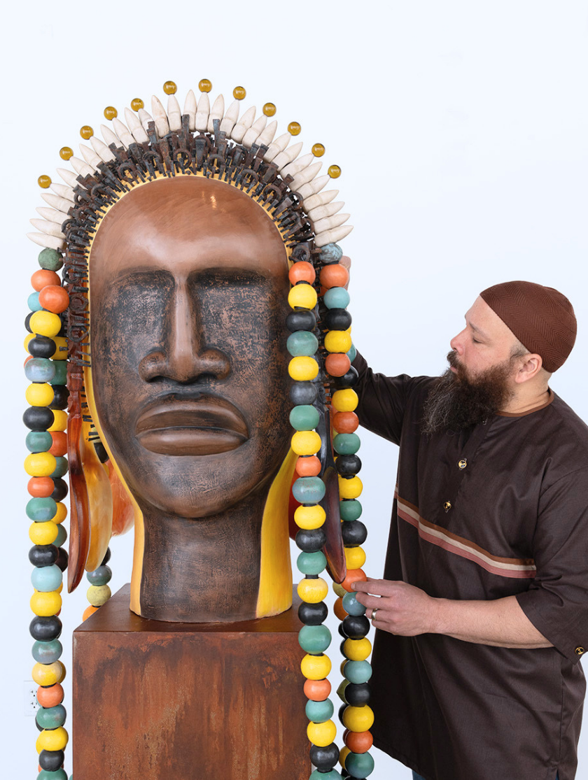 A man adjusts a large, beaded, sculpted head wearing a colorful beaded headdress.