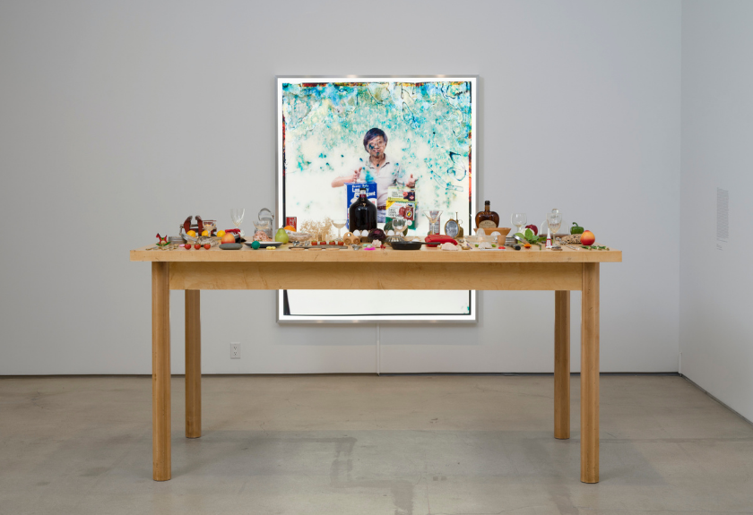 A wooden table with assorted food items, set in front of a large framed portrait on the wall.