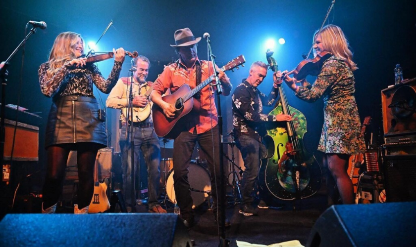 Five musicians perform on stage with string instruments under blue lighting.
