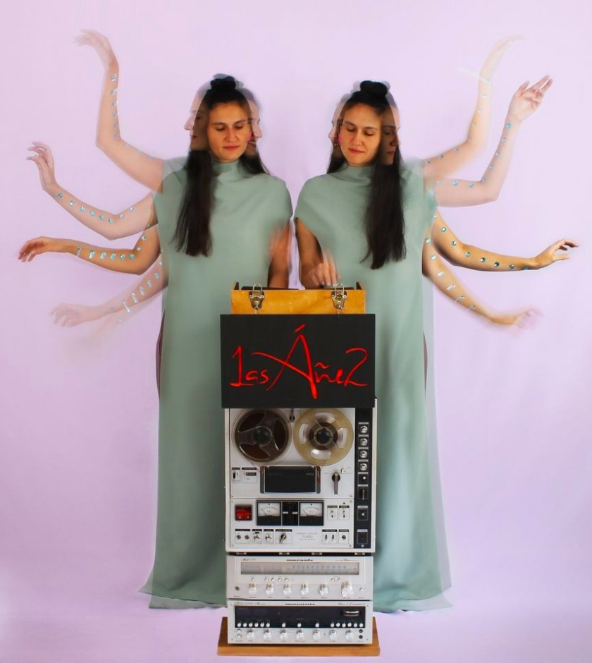 Two women in green dresses stand by audio equipment, arms blurred to show movement.