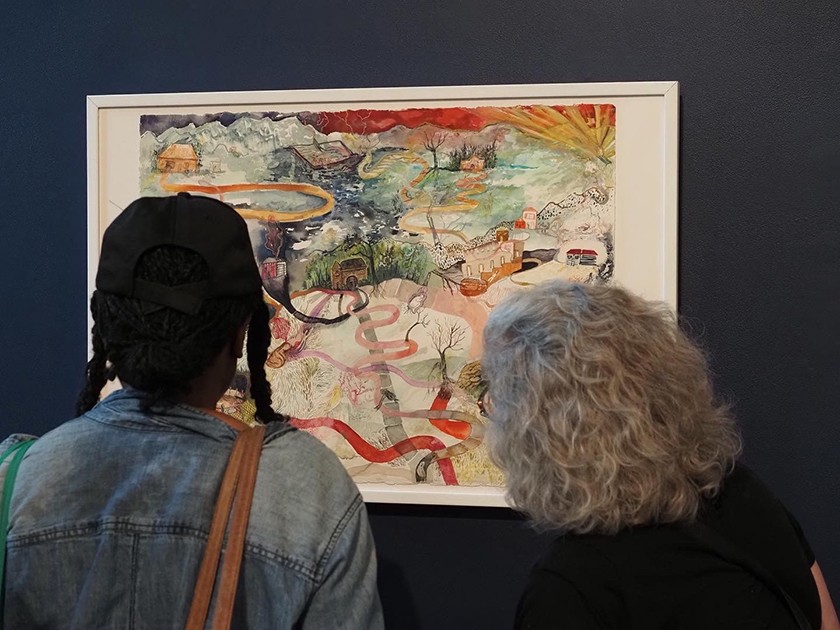Two people stand with their backs to the camera, looking at a framed colorful artwork hanging on a dark wall